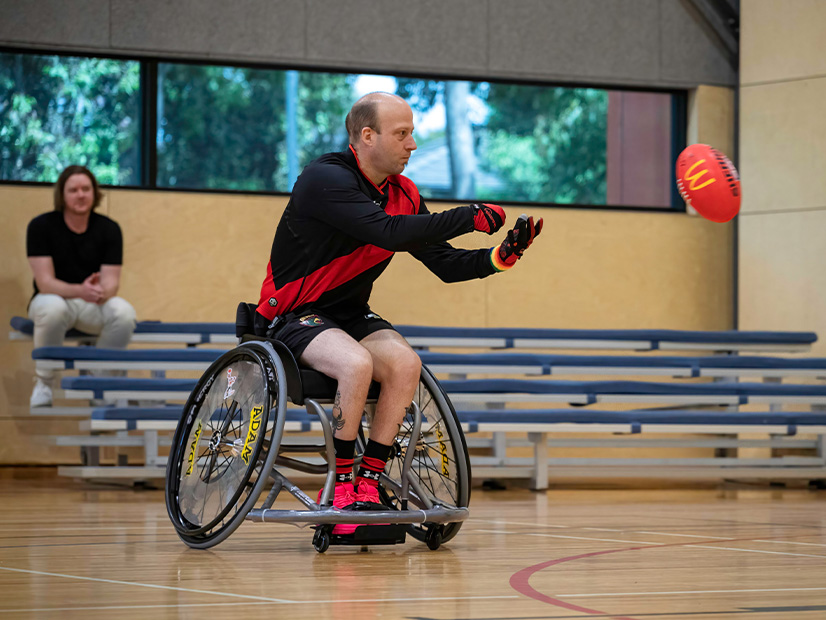 Man in wheelchair handballing a football